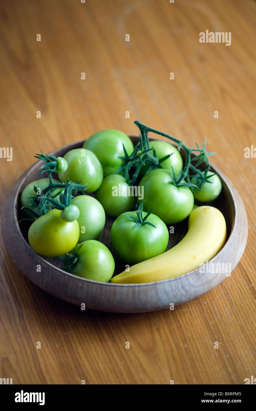 Grüne Tomaten in Schüssel neben Bananen Stockfoto