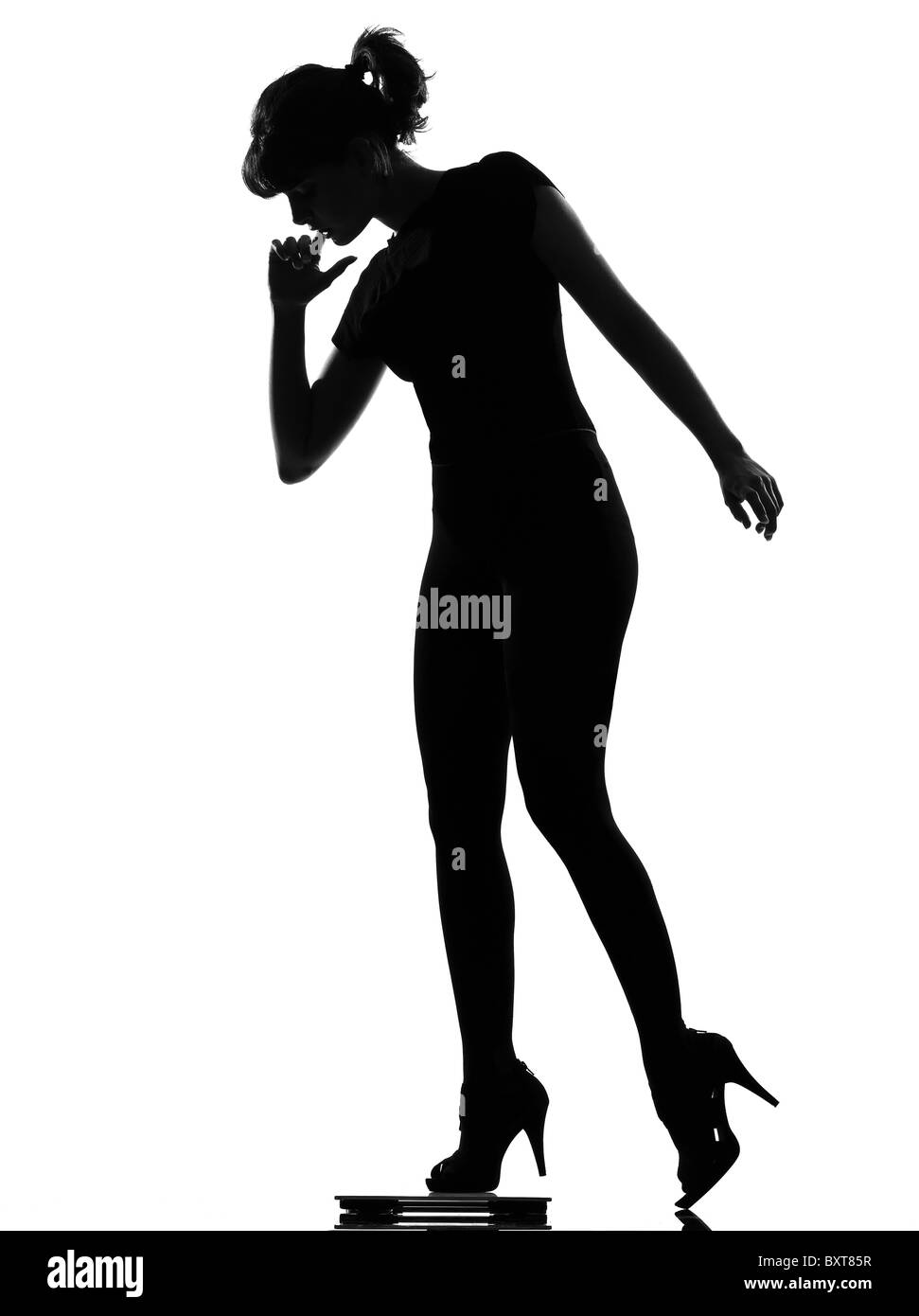 voller Länge Silhouette im Schatten einer jungen Frau, die verstärkt auf persönliche Badezimmerwaage im Studio auf weißen Hintergrund isoliert Stockfoto
