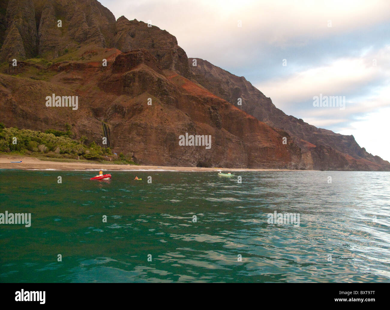 Blick auf Kalalau Strand und Wasserfall aus dem Wasser im frühen Morgenlicht mit einem Schlauchboot und Kajak in der Nähe, Na Pali, Kauai Stockfoto