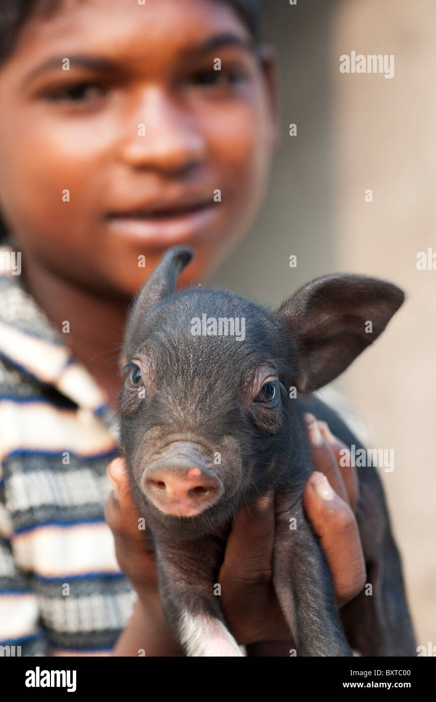 Untere Kaste indischer Junge mit kleinen Schwein, das von ihm aufgezogen wird und verkauft für Fleisch, wenn völlig gewachsen. Andhra Pradesh, Indien Stockfoto