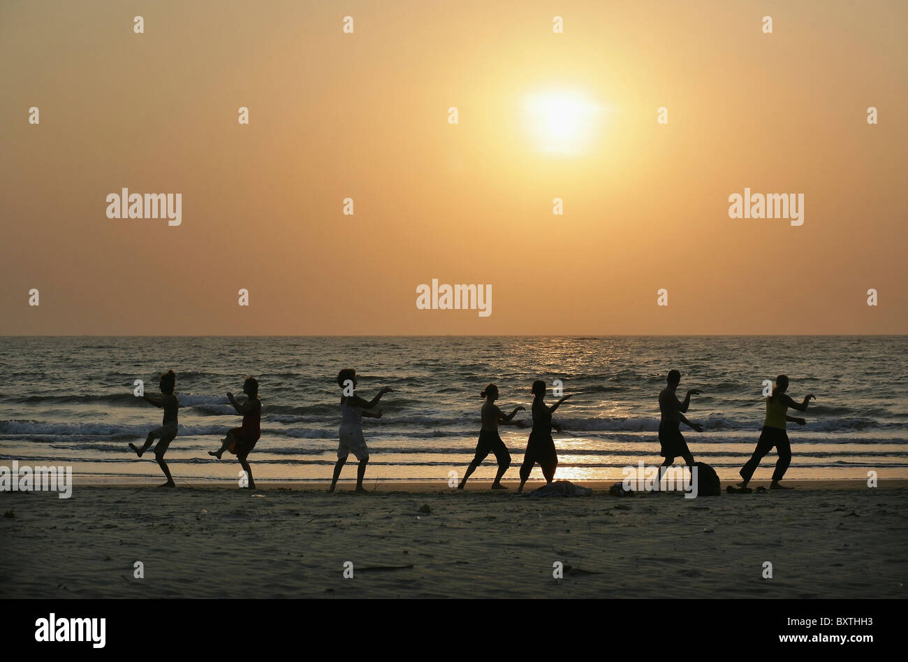 Silhouetten von Menschen, die Tai Chi am Meer am Strand bei Sonnenuntergang Stockfoto