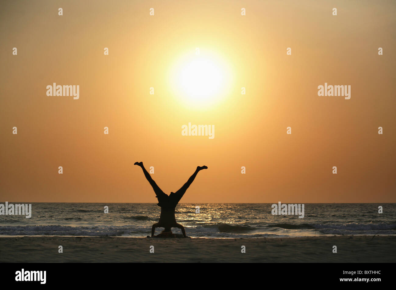 Silhouetten der Mann tut Yoga vom Ozean am Strand bei Sonnenuntergang Stockfoto