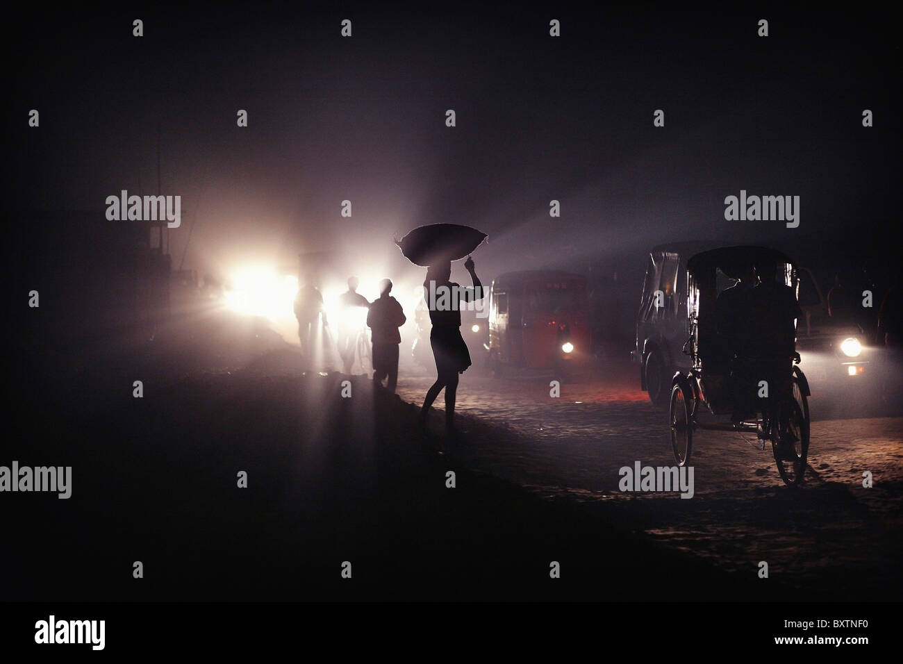 Silhouetten von Verkehr und Menschen, die Säcke auf ihren Köpfen in der Nacht Stockfoto