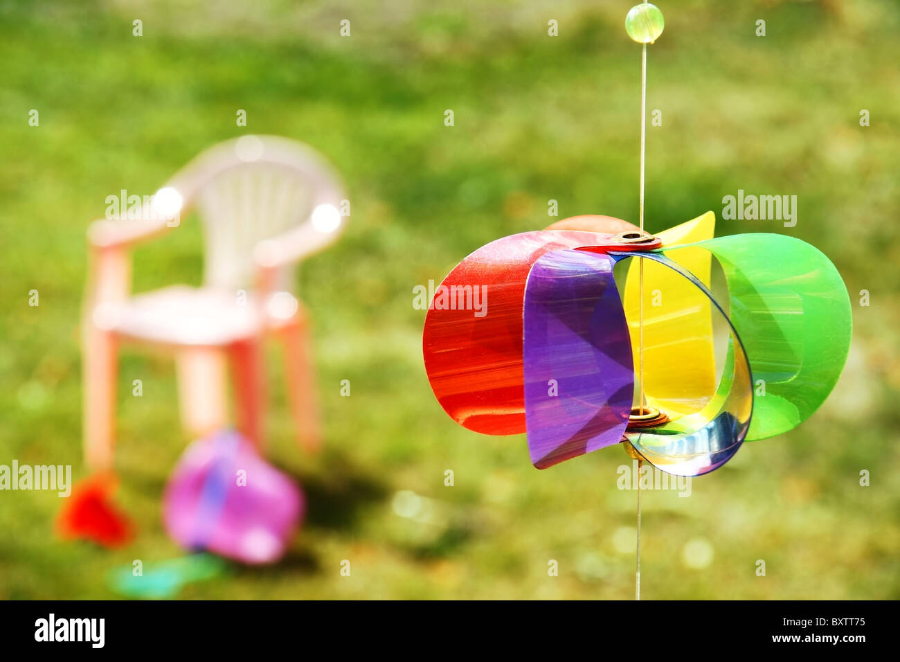 Kind Spielzeug verstreut auf dem Rasen im Garten mit bunten Windrad Wind Spielzeug im Vordergrund. Stockfoto