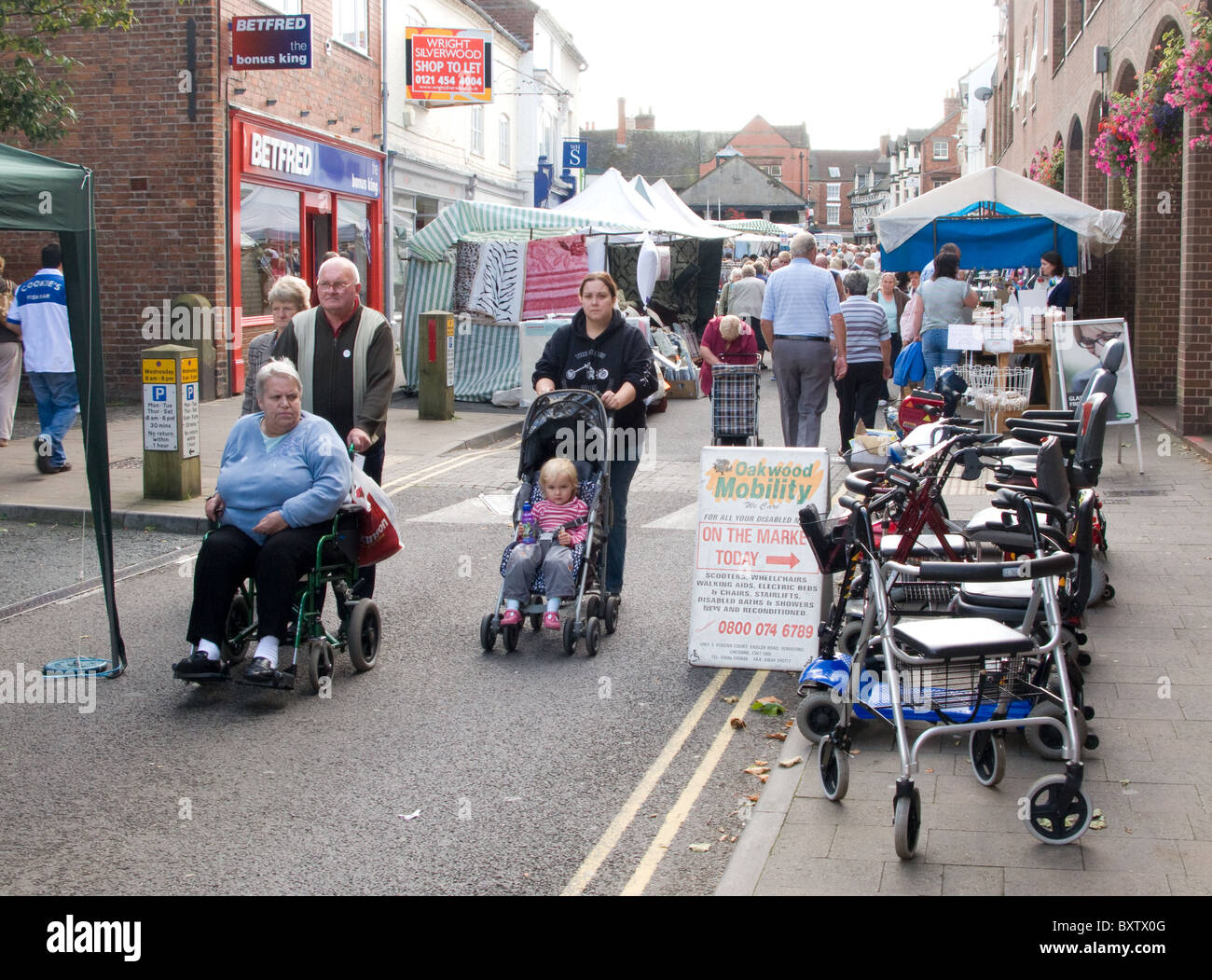 Ein Erwachsener in einem Rollstuhl und ein Kind im Kinderwagen, neben einem Marktstand verkaufen Mobilitätshilfen. Stockfoto