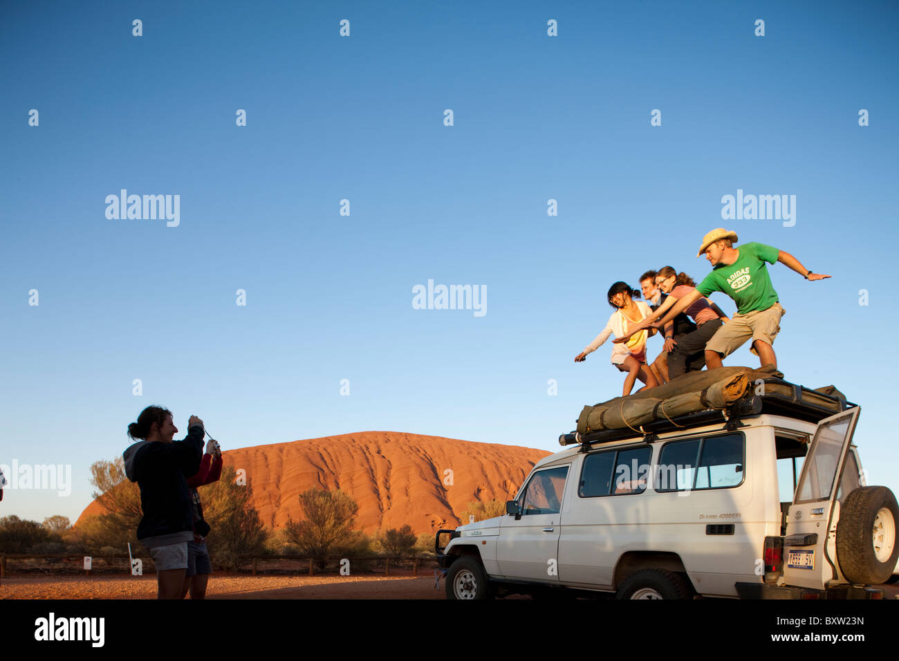 Australien-Northern Territory Uluru - Kata Tjuta National Park junge Touristen Post für Schnappschüsse wie steigende Sonne leuchten Ayers Rock Stockfoto