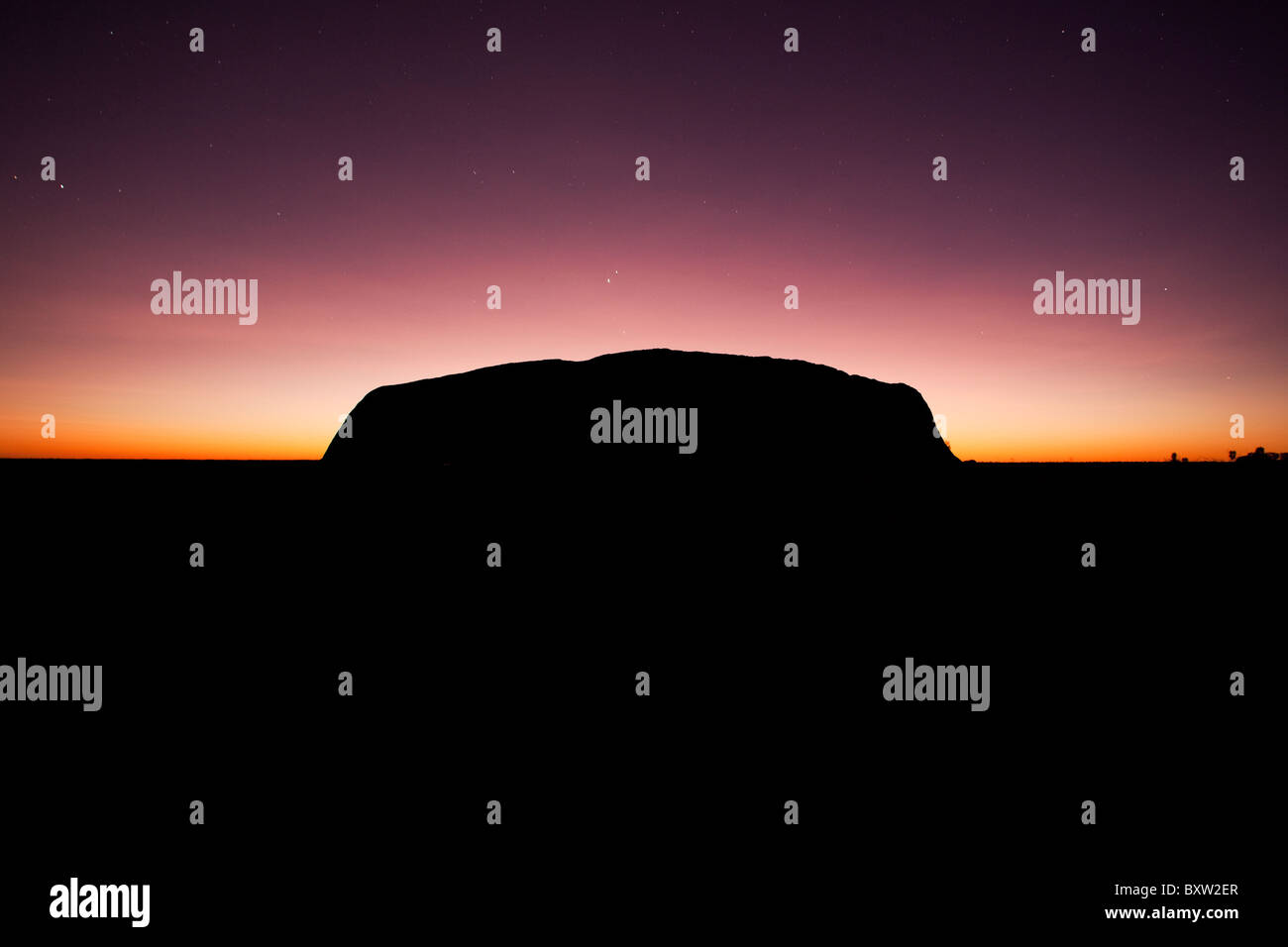 Australien, Northern Territory, Uluru - Kata Tjuta National Park, Rising Sun Silhouetten Ayers Rock vor der Morgendämmerung am Sommermorgen Stockfoto
