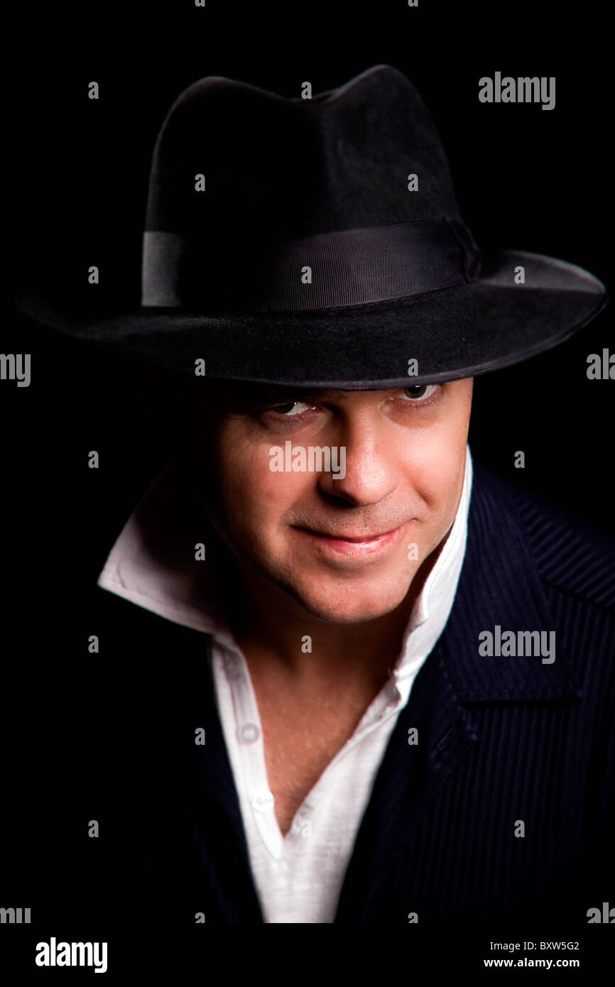 Ein reifer männlicher Künstler Sänger mit einer schwarzen Fedora Hut und blau Wildlederjacke gestellt, Blick in die Kamera selbstgefällig und Inhalte Stockfoto