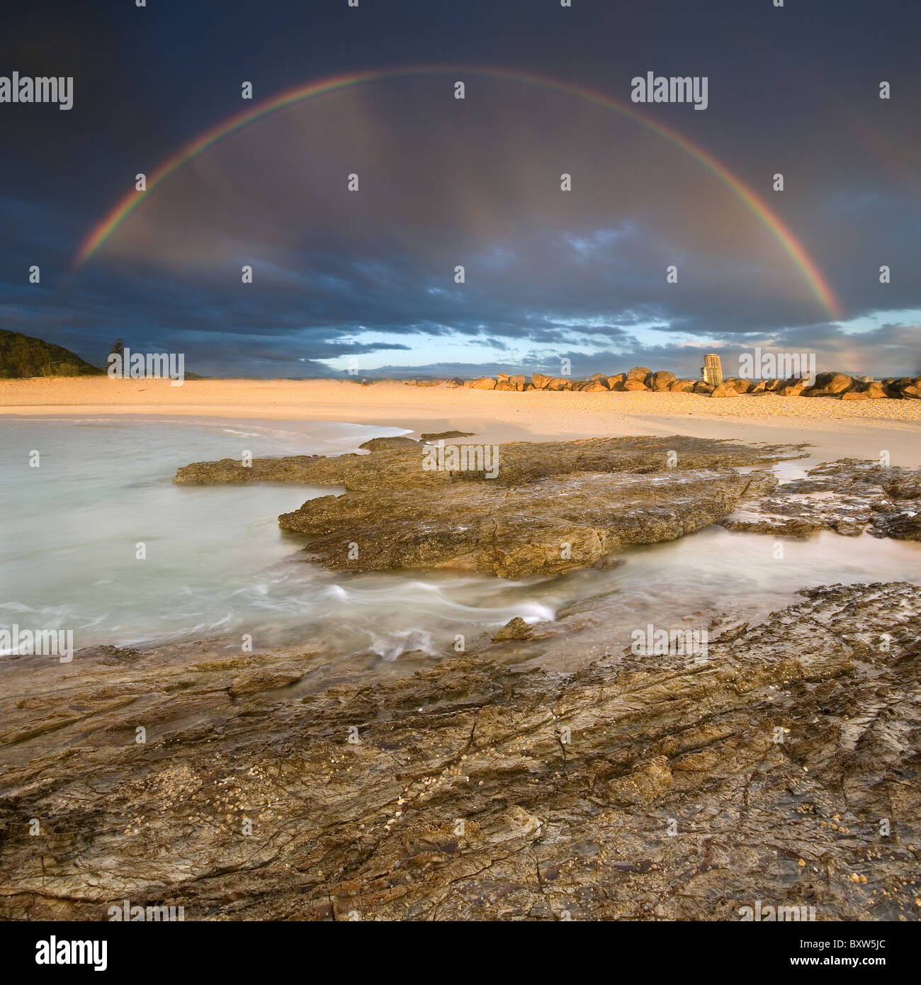 Regenbogen mit Felsen im Vordergrund am bewölkten Morgen Stockfoto