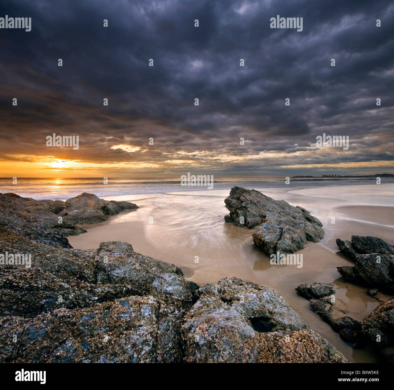Felsen am Strand bei Sonnenaufgang mit dramatischer Himmel auf ein quadratisches format Stockfoto