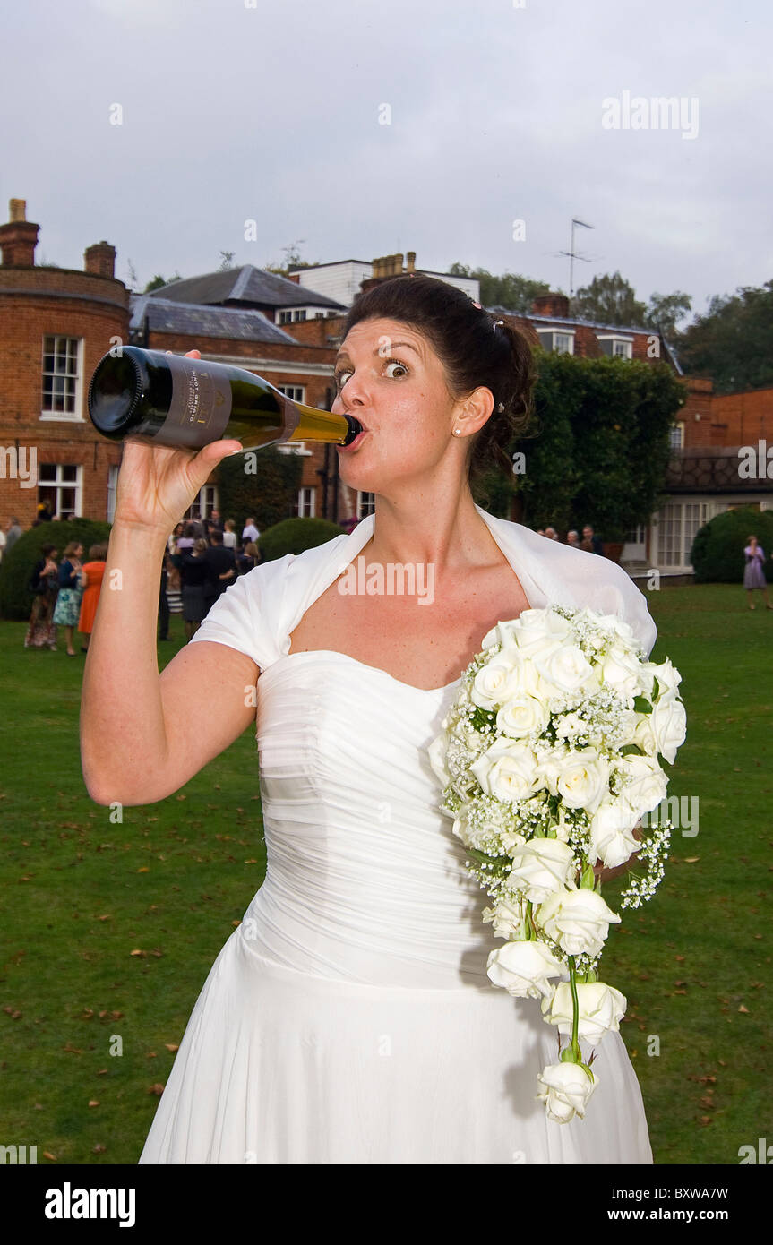 Vertikale nahe Porträt einer Braut an ihrem Hochzeitstag heimlich ein schnelles Getränk direkt aus einer Flasche Champagner. Stockfoto