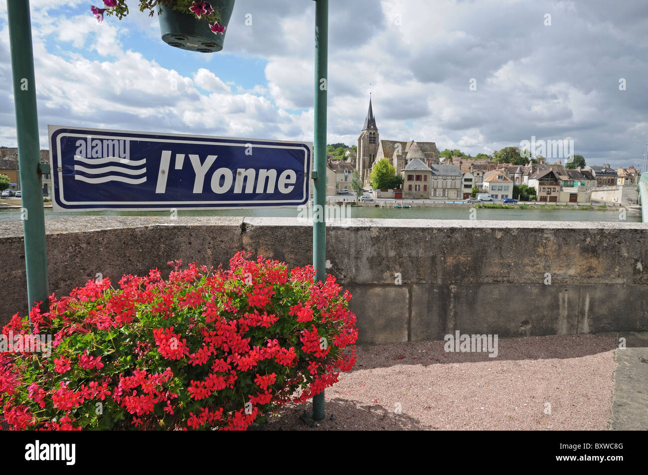 Fluss-Schild am Pont Sur Yonne Burgund Frankreich mit Blumenkörben Geranien im Vordergrund und Kirche eglise Stockfoto