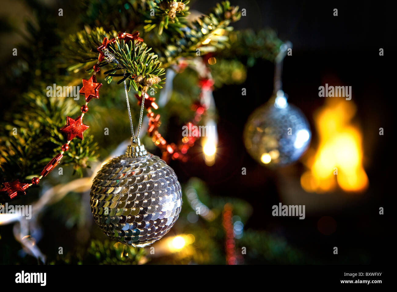 Disco Spiegel Kugel Dekorationen hängen von einem Weihnachtsbaum vor einem Feuer am Heiligabend Stockfoto