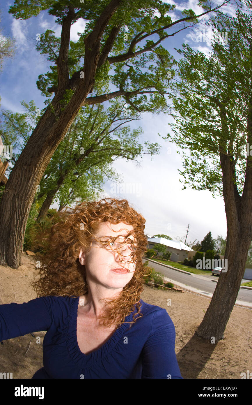 Frau mit roten lockiges Haar weht im Wind, Bäume im Hintergrund, Fish-Eye-Objektiv. Stockfoto