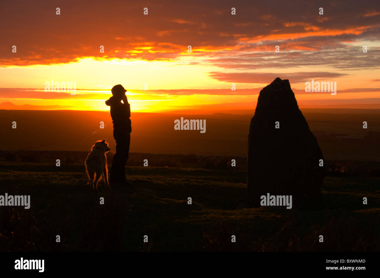 Junge Frau mit Hund durch den Stein auf dem Hügel Rigifa "bei Sonnenuntergang.  In der Nähe von Mey, Thurso, Caithness, Schottland Stockfoto