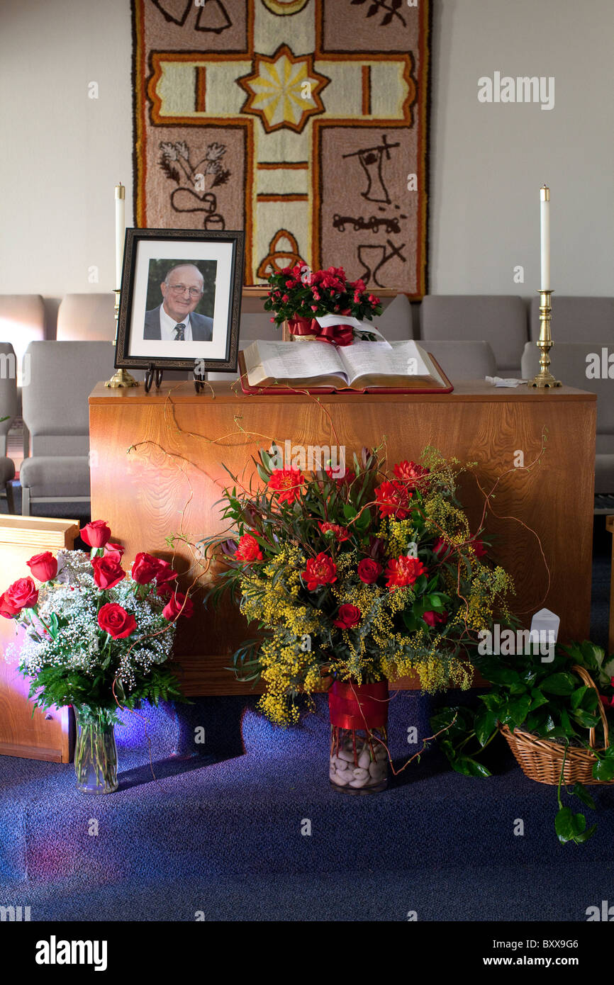 Rosen und andere Blumenarrangements zieren Altar, gekrönt von einem Foto des Verstorbenen, während einer Trauerfeier in der Kirche Stockfoto