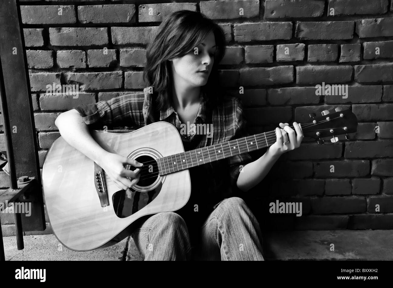 Schwarz / weiß Bild der Gitarristin Geklimper Gitarre beim sitzen und Ziegelwand gelehnt. Stockfoto