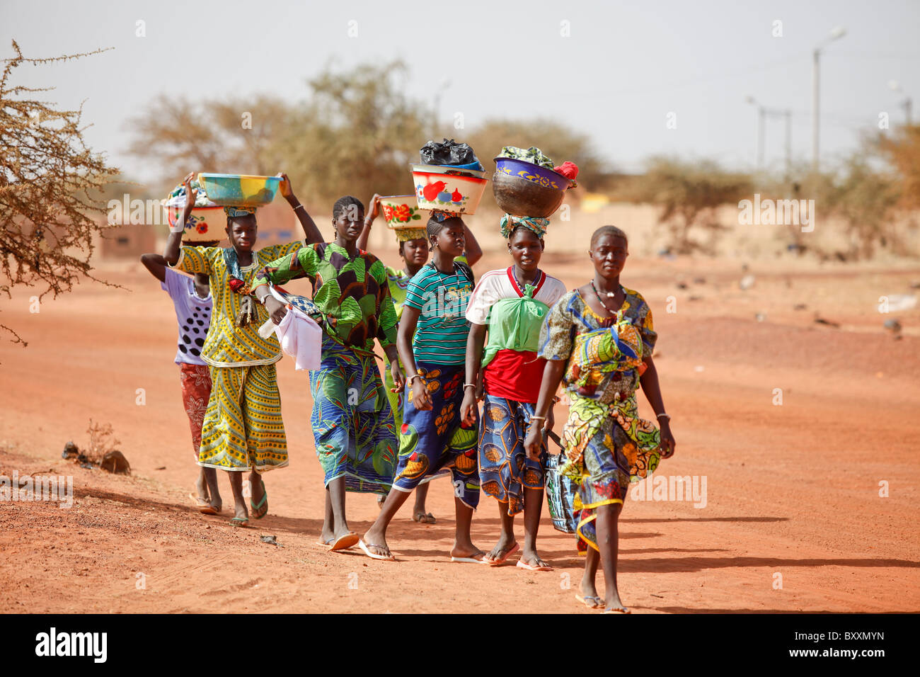 Frauen kommen in die Stadt Djibo, Burkina Faso, zu Fuß, ihre waren auf ihren Köpfen in traditionelle afrikanische Mode tragen. Stockfoto