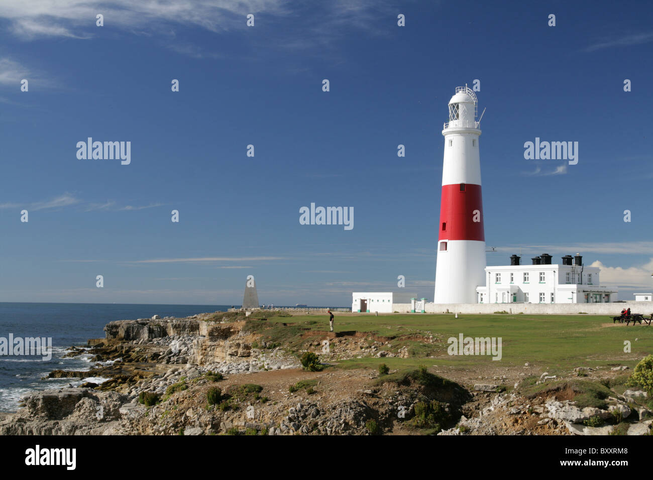 Portland Bill Leuchtturm in weiß und rot vor blauem Himmel, mit Meer und Felsen. Stockfoto