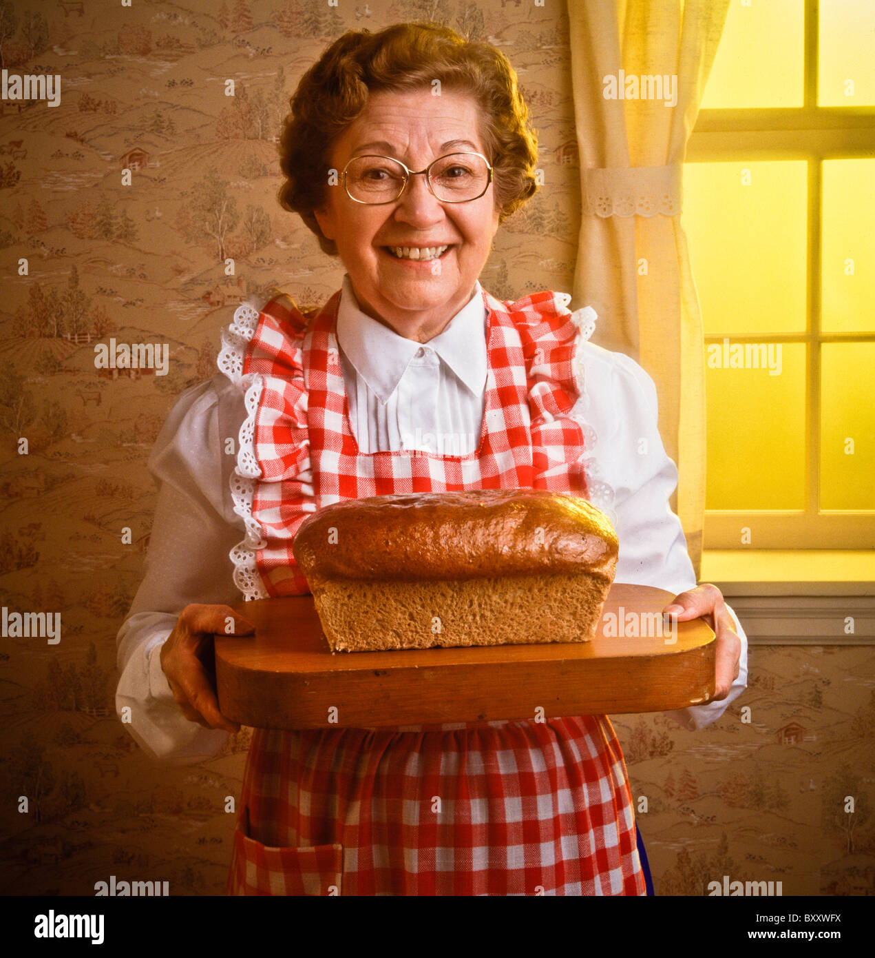 Eine ältere Senioren Landwirte Frau zeigt frisch gemachte Brotlaib auf Schneidebrett. Am frühen Morgen Fensterlicht Stockfoto