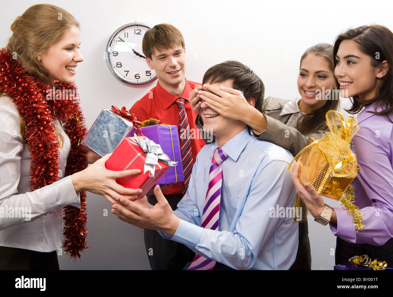 Foto von fröhlichen Geschäftsfrau, halten sie die Hände auf den Augen des Mannes während ihrer Kollegen bereitet Geschenke für ihn Stockfoto