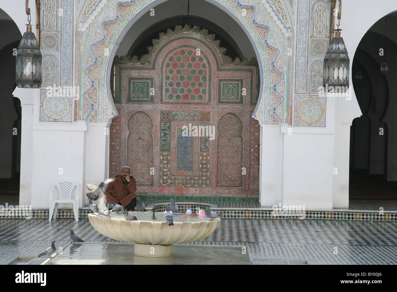 ein muslimischer Mann in Fes Marokko sitzen in einem ummauerten Bereich einer Moschee schlagt einige Tauben fliegen aus einem Brunnen in einem alten Stockfoto