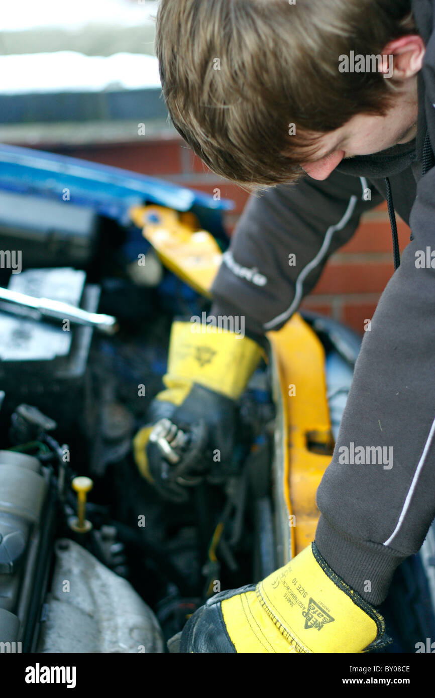 Einen jungen kaukasischen männlichen Mechaniker arbeitet unter der Motorhaube eines Autos, Schutzhandschuhe tragen. Stockfoto