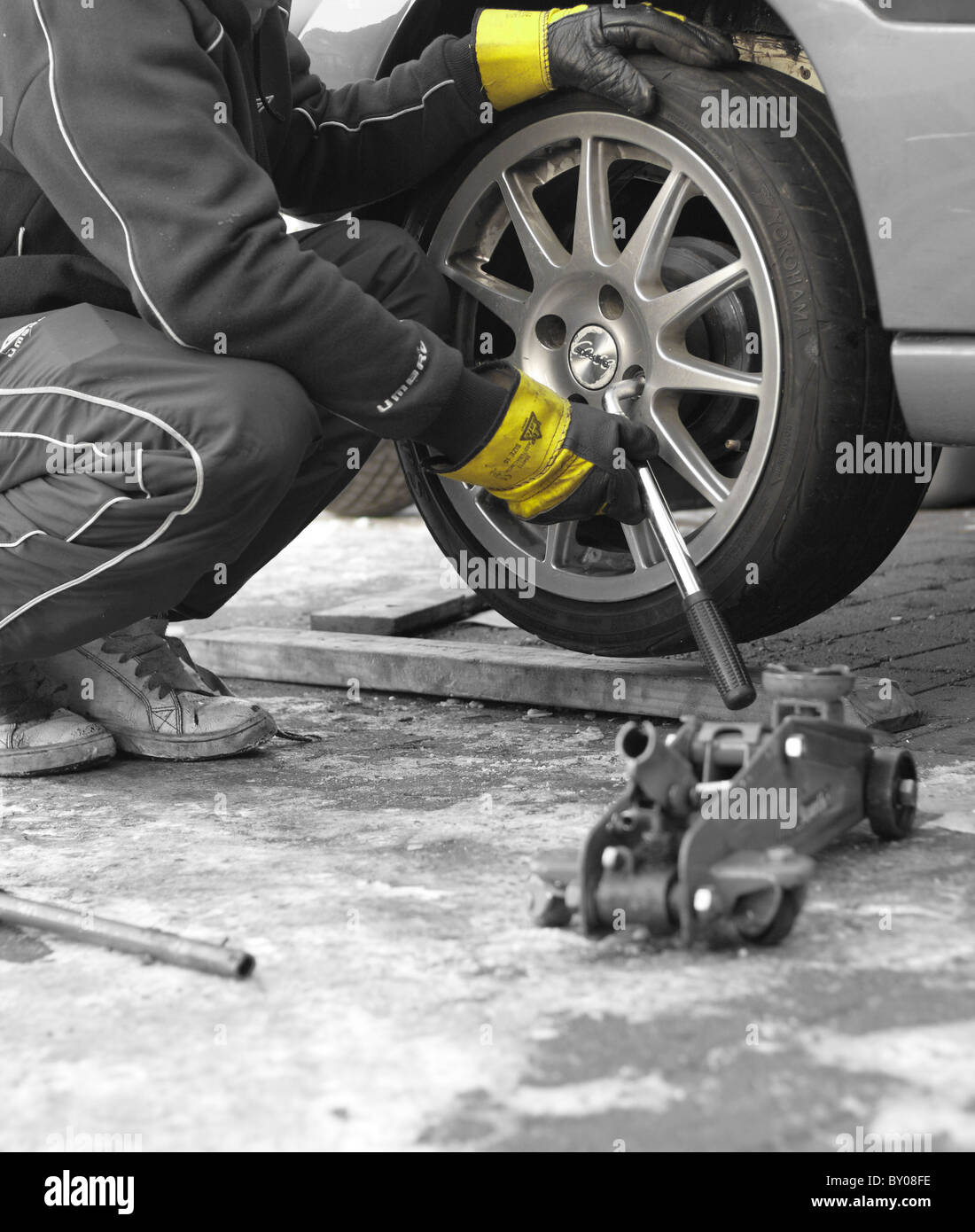 Ein Mechaniker die Radmuttern mit einem Schraubenschlüssel abschrauben, das Rad von einem Auto, Rigger Handschuhe zum Schutz zu entfernen. Stockfoto