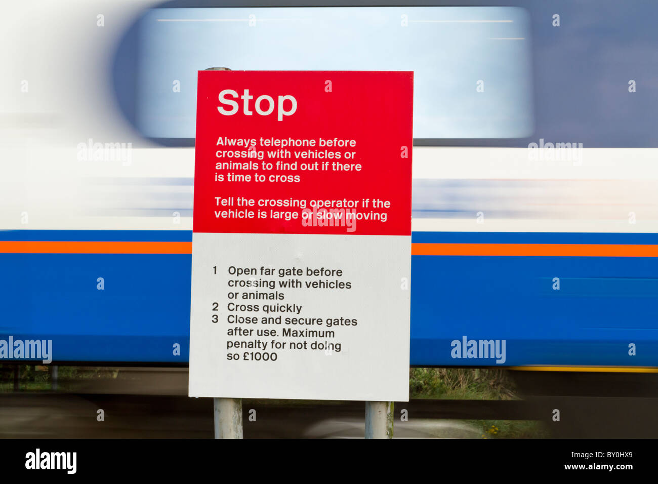 Warnhinweis. Schnelle Zug passiert ein Stoppschild in einem ungeschützten Bahnübergang auf einer Bahnstrecke in Nottinghamshire, England, Großbritannien Stockfoto