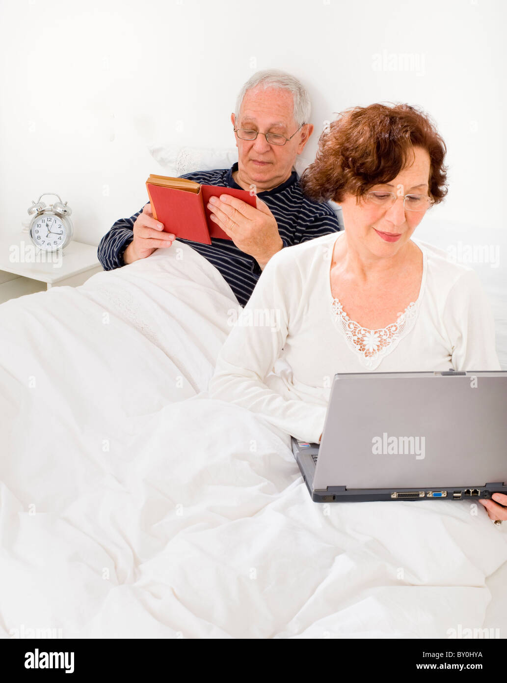 Älteres Paar im Bett mit Laptop und Buch Stockfoto