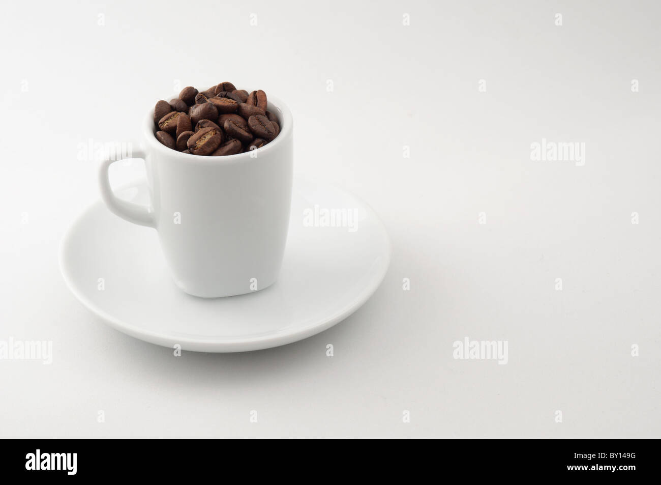 Eine Espresso-Tasse mit Kaffeebohnen gefüllt sitzt auf eine Untertasse. Vor neutralem Hintergrund fotografiert. Stockfoto