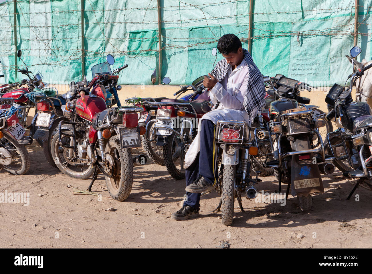 Ägyptischen Mann sitzt auf Motorrad geparkt außerhalb der Kamel- und Vieh Wochenmarkt in der Nähe von Luxor, Ägypten Stockfoto