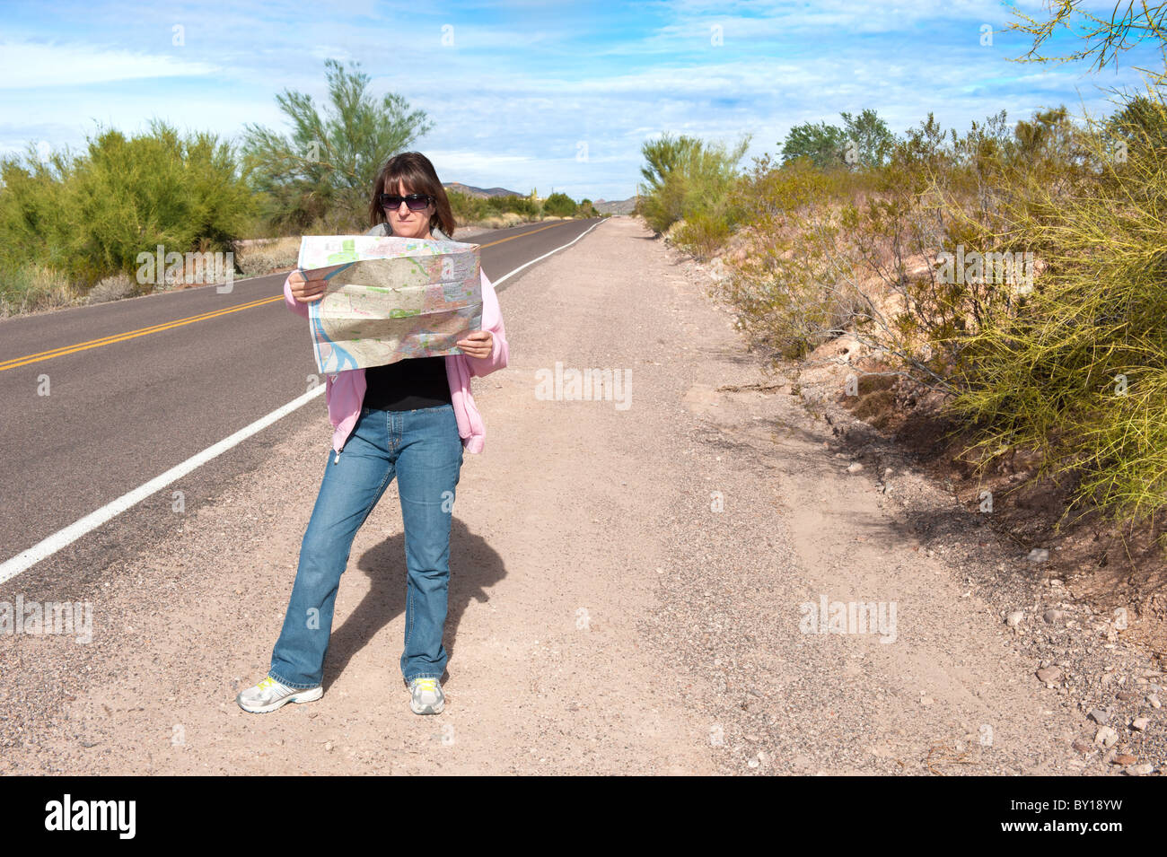 Eine Frau steht an der Seite eine abgelegene verlassene Straße Kartenlesen. Stockfoto