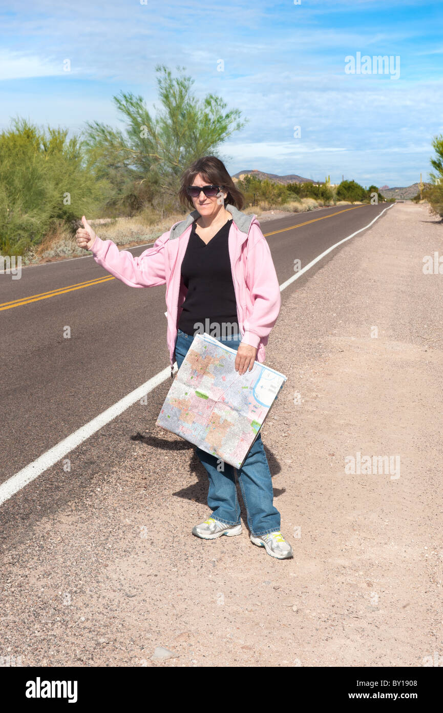 Eine Frau, die eine Karte hitchhikes auf einem abgelegenen Wüste Straßenrand. Stockfoto