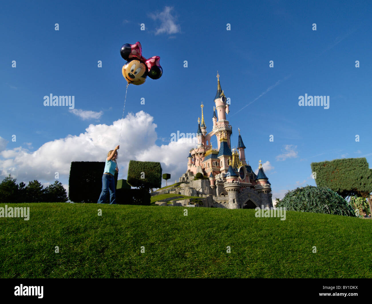 Kleines Mädchen mit Mickey-Mouse-Ballon auf einer Wiese vor dem schlafenden Schönheit Schloss in Eurodisney, Paris, Frankreich Stockfoto