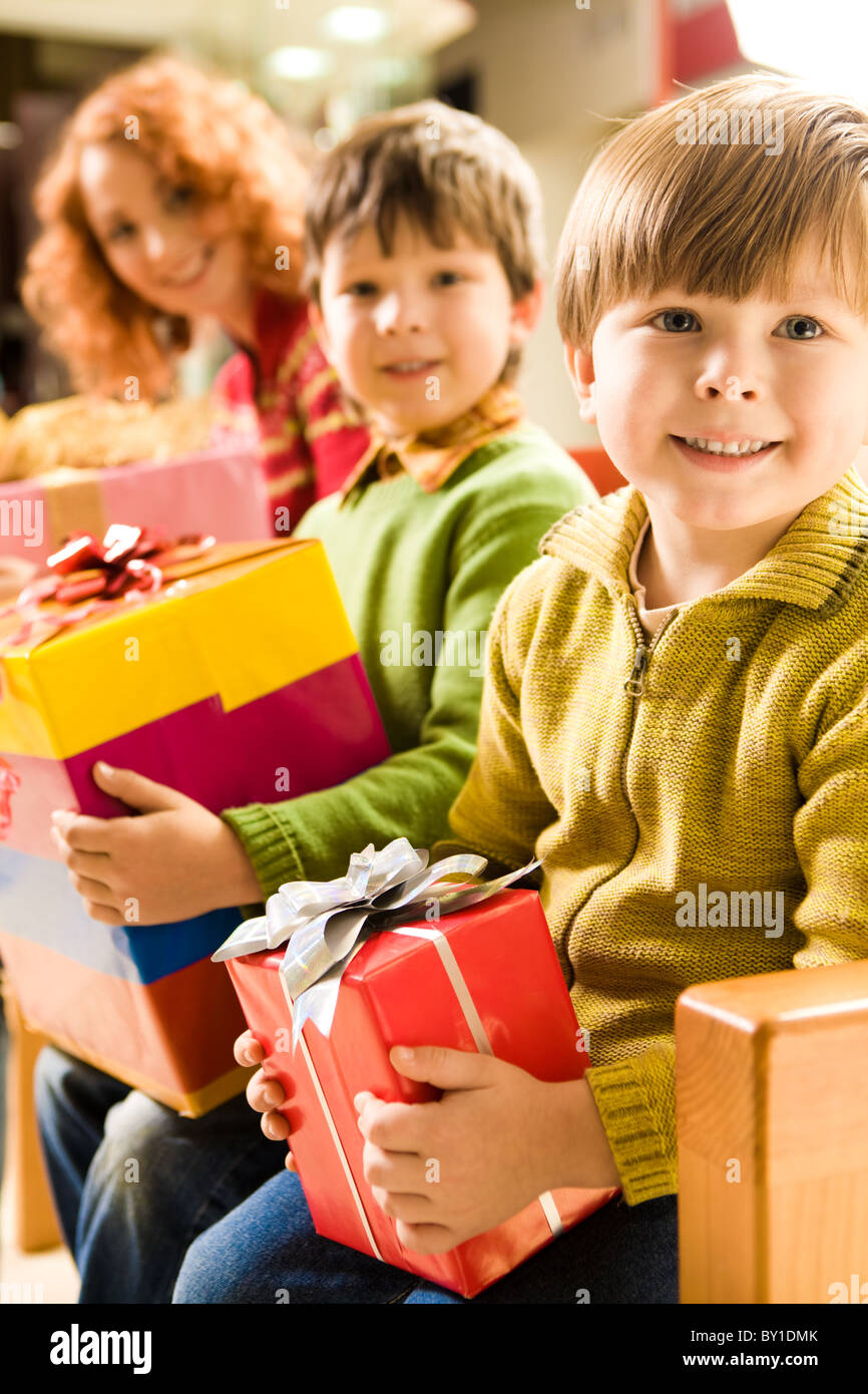 Fröhlicher Junge mit Geschenk in Händen sitzen im Supermarkt auf Grund von seinem Bruder und seiner Mutter Stockfoto