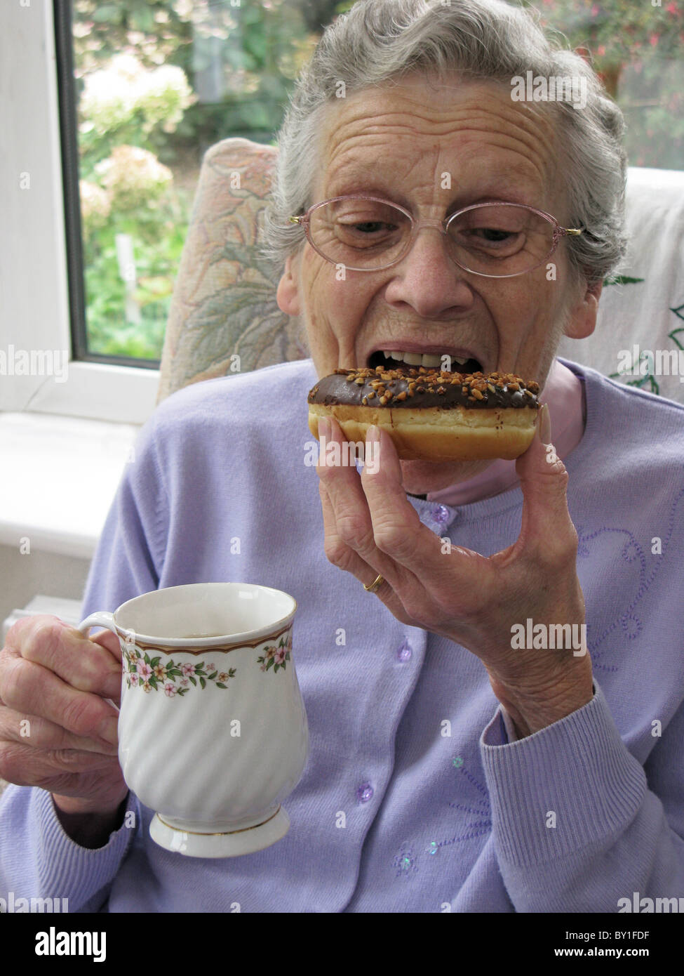 ältere Frau zum Anbeißen aus einem Schokolade überdachten Donut an teatime Stockfoto