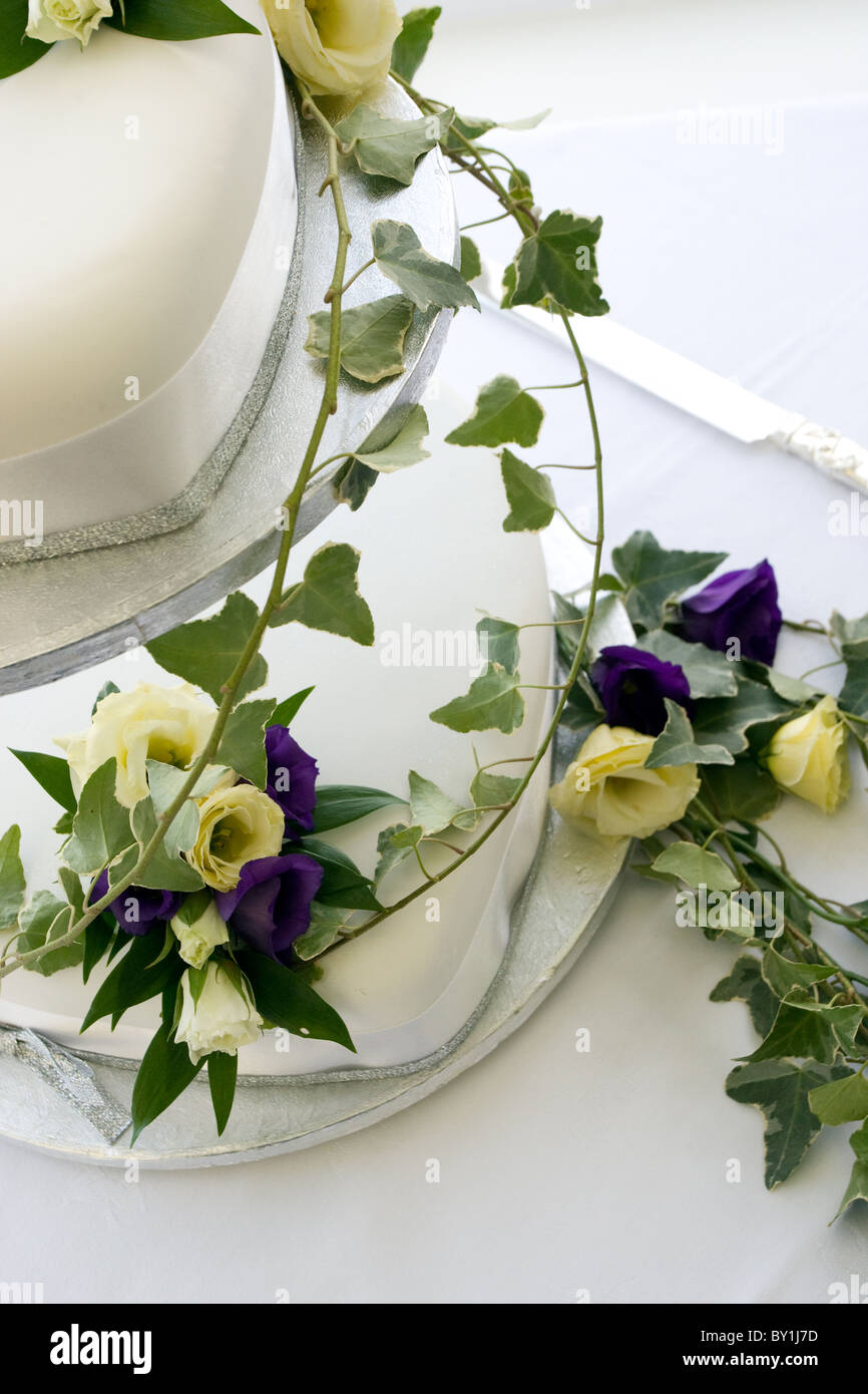 Zweistufigen weiße Hochzeitstorte drapiert in lila und Creme Blüten mit Efeu Stockfoto