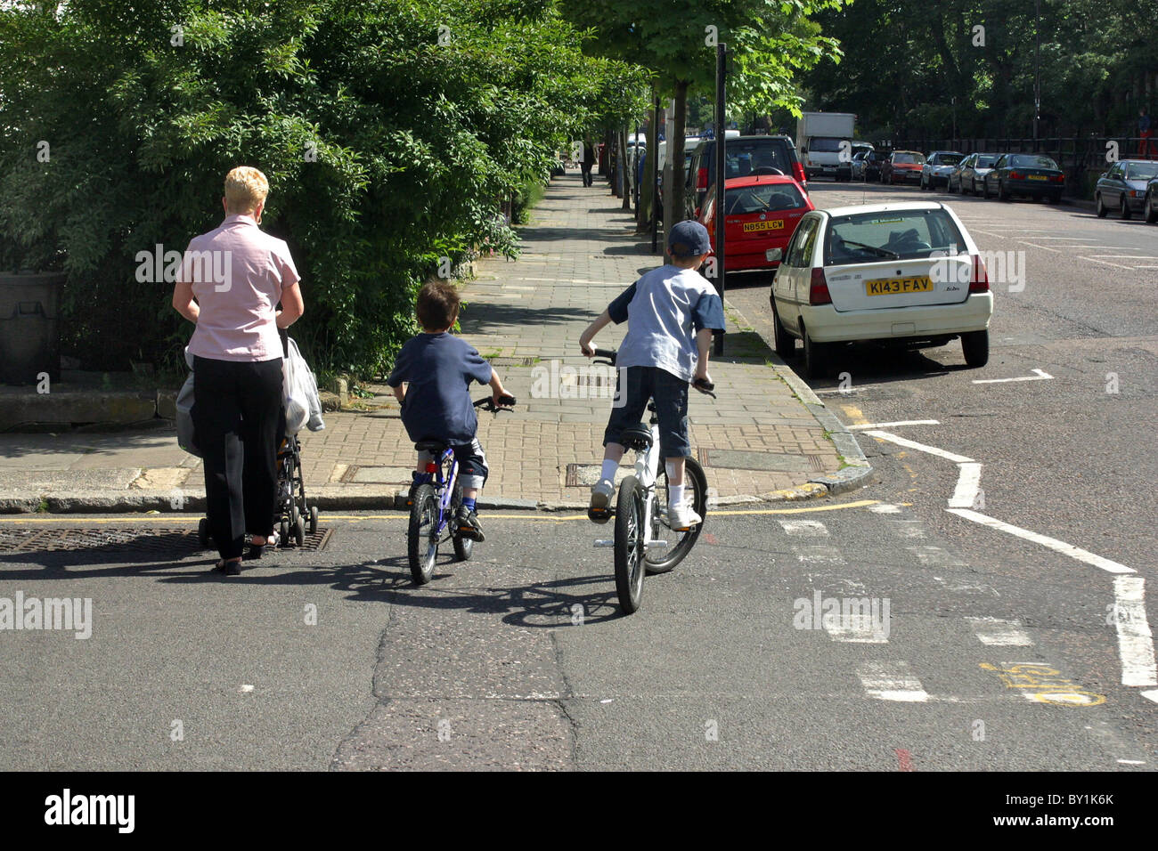 Kinder auf dem Fahrrad reiten neben Mutter mit Kinderwagen Stockfoto