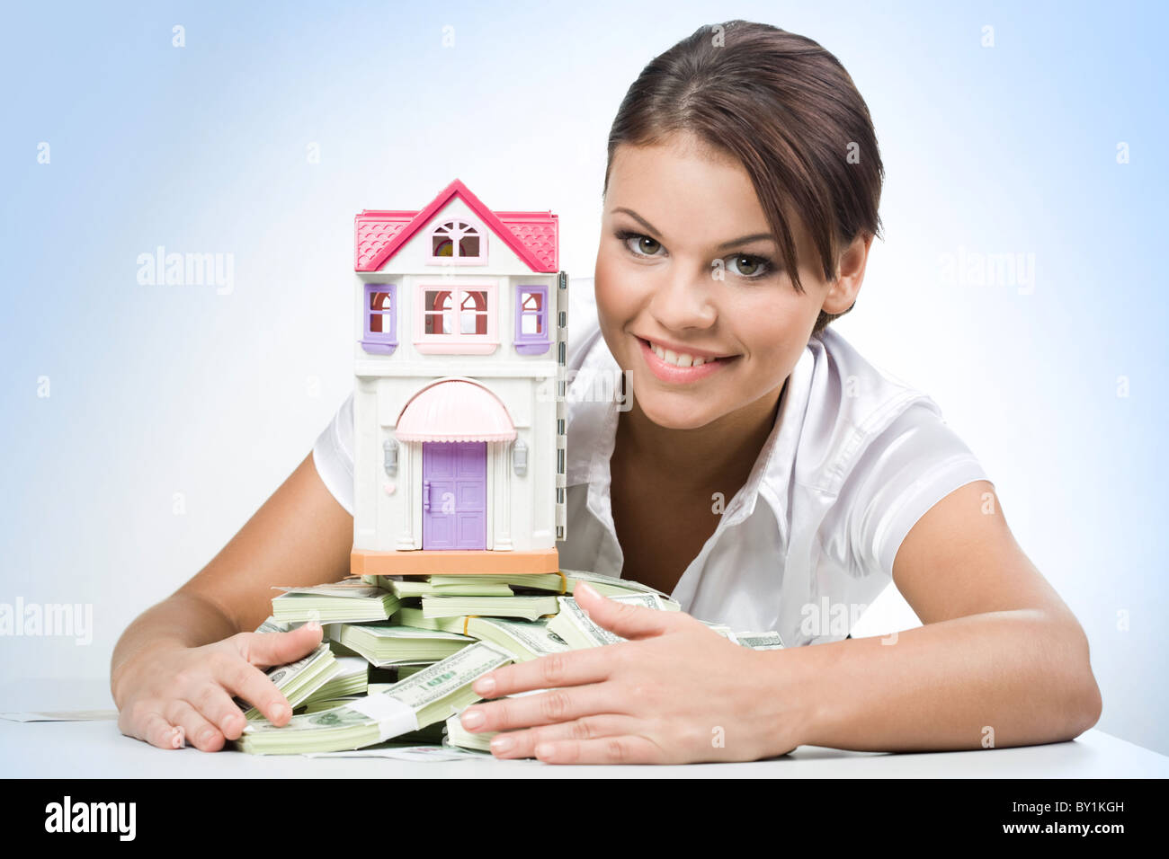 Porträt der schönen Frau Haufen des Geldes mit Spielzeug Haus auf seiner Spitze zu berühren Stockfoto