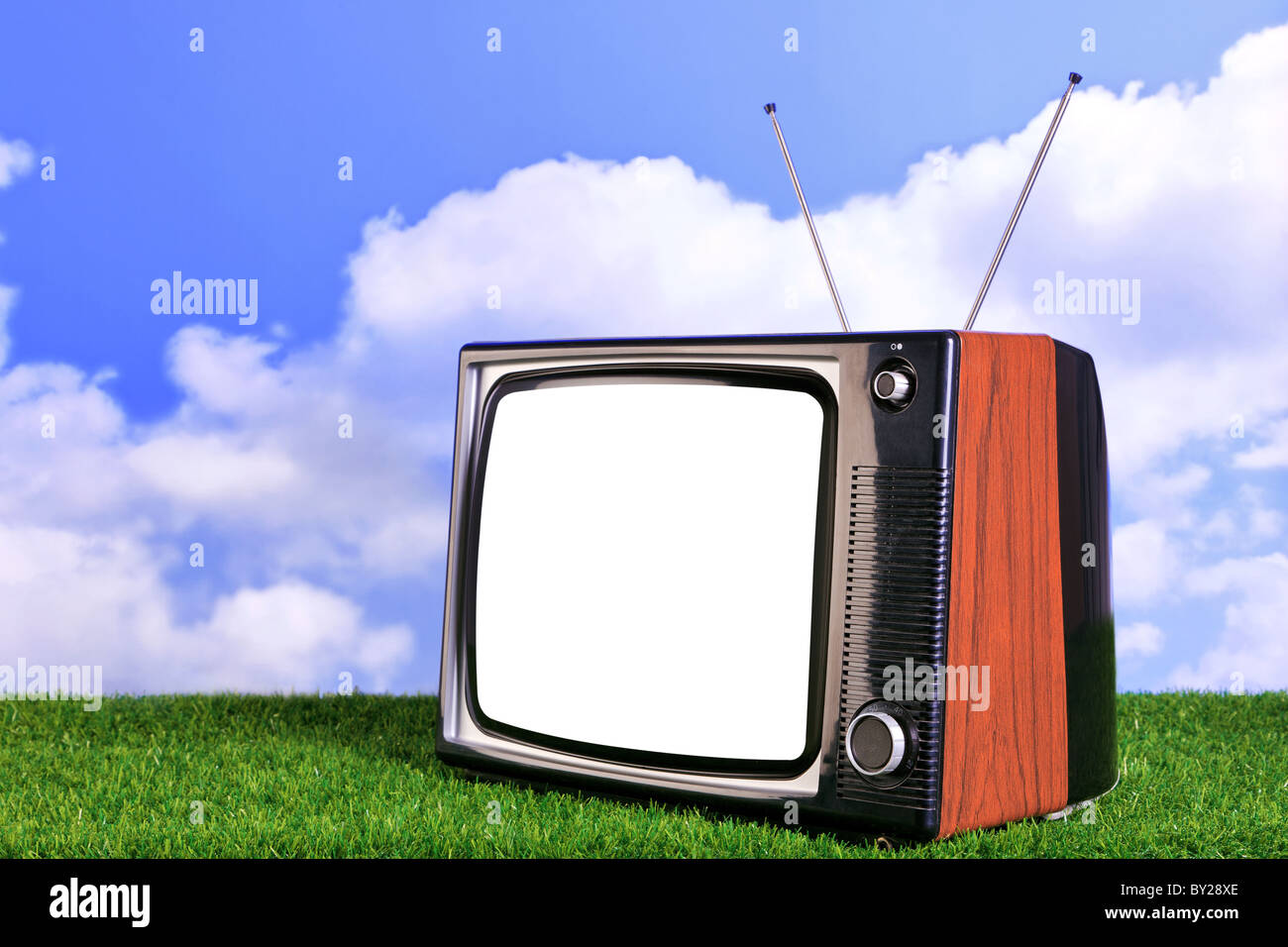 Foto von einem alten Retro-TV im Freien auf dem Rasen mit blauem Himmel und weißen Wolken im Hintergrund Stockfoto
