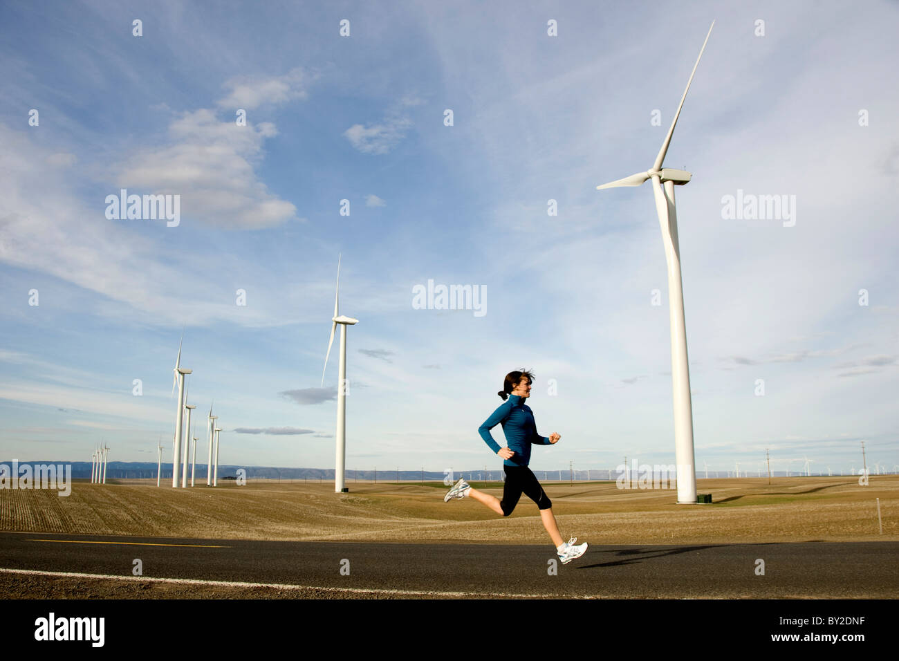 Eine Frau, Joggen auf einer Straße mit Windmühlen drehen im Hintergrund. Stockfoto