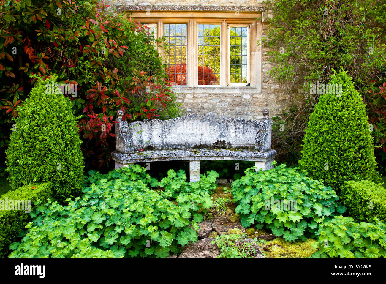 Eine Steinbank unter einer zweibogigen Fenster einer abgelegenen Ecke des einen englischen Country-Sommergarten Stockfoto