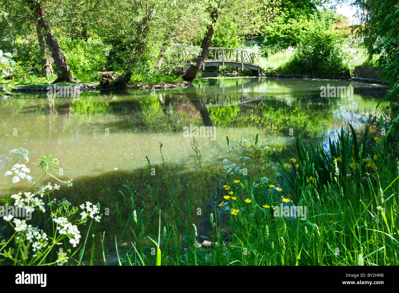 Ein großer Zierteich oder kleiner See mit einem rustikalen Holzbrücke in einem englischen Landhaus-Garten im Sommer Stockfoto