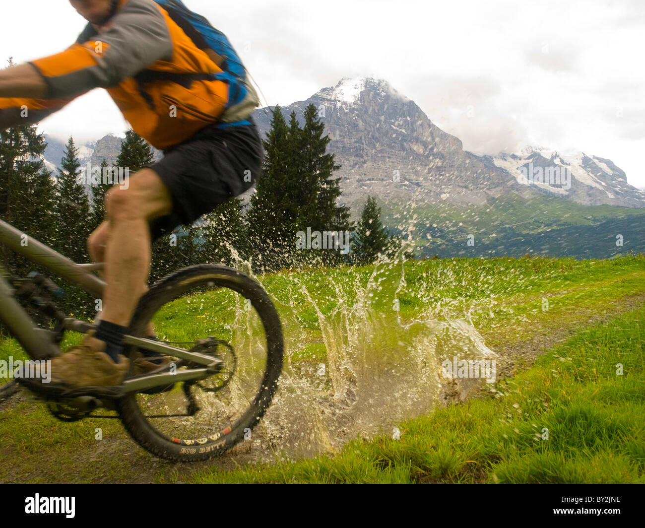 Ein Mountainbiker fährt durch eine Schlamm-Pool auf dem Radweg in Richtung erste. Im Hintergrund den Eiger. Stockfoto