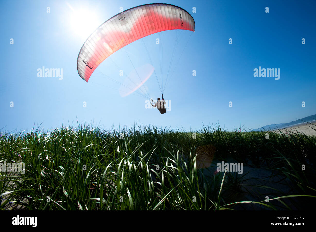 Niedrigen Winkel Perspektive von einem männlichen Gleitschirm fliegen über Gras- und Strand in schönes Licht. Stockfoto