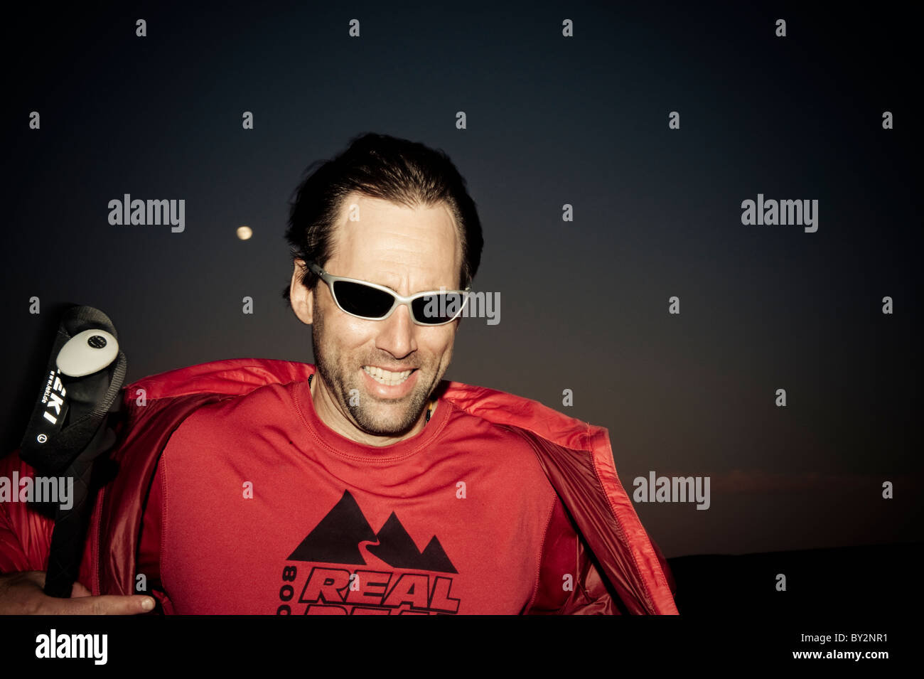 Porträt eines blinden Athleten lehnt sich gegen den Wind in der Dämmerung mit einem Vollmond. Stockfoto