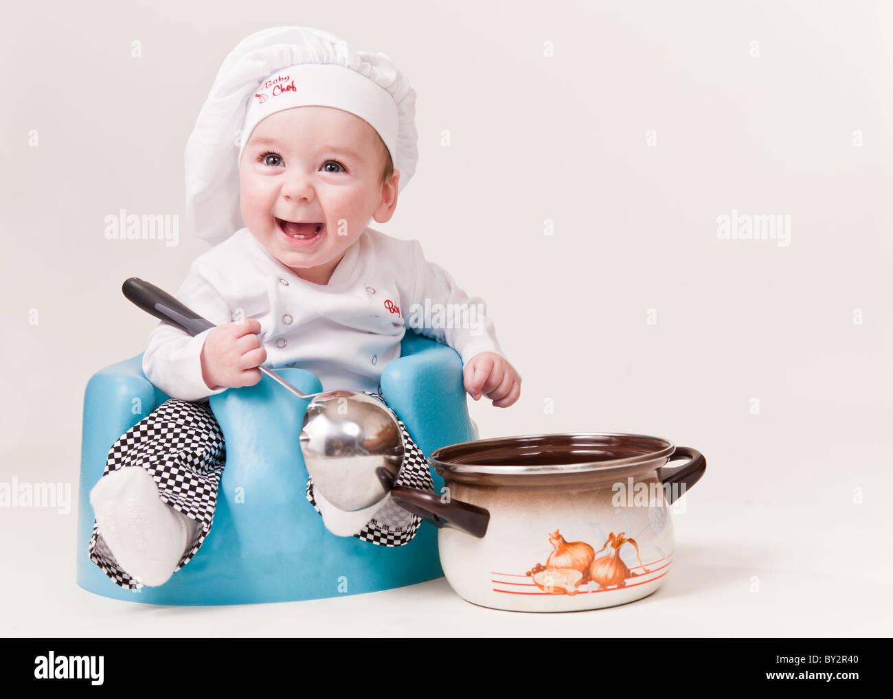 Baby-Chef sitzt neben Suppentopf tragen Koch ist einheitlich und lächelnd. Stockfoto