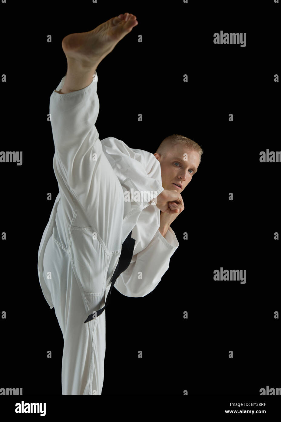 Junger Mann, die Durchführung von Karate Kick auf schwarzem Hintergrund Stockfoto