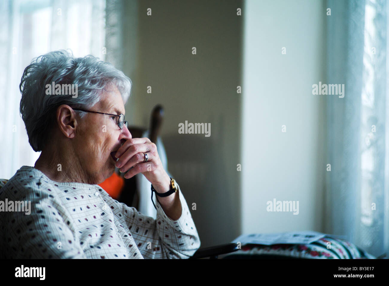 Alte Frau sitzt im Stuhl mit Hand in den Mund. Stockfoto